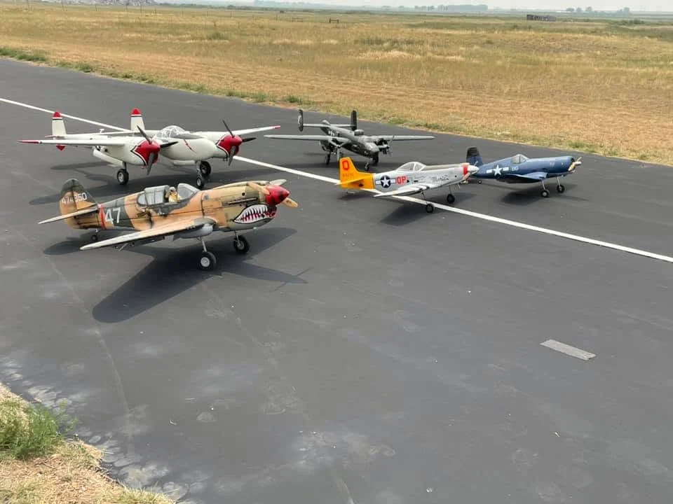 Several radio-controlled aircraft parked together on the paved runway